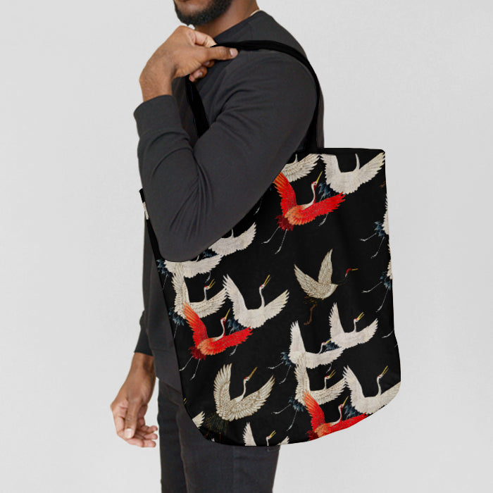 Person carrying a black tote bag with colorful bird pattern on a light gray background