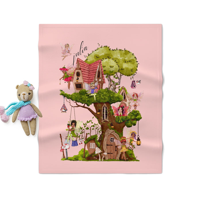 Children's blanket with fairy tale design featuring tree houses and fairies on a pink background.