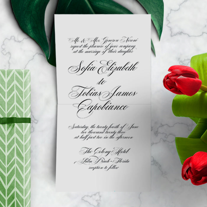 Wedding invitation card with green patterned envelope on a marble surface with red tulips.