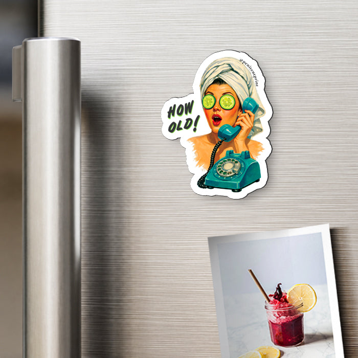 A die-cut magnet featuring a retro-style illustration of a woman with cucumber eyes and a teal rotary phone, with the text 'HOW OLD!', shown attached to a stainless steel refrigerator next to a printed photo.