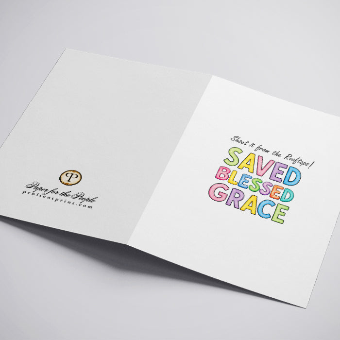 A white greeting card with the text 'Shout it from the Rooftops! SAVED BLESSED GRACE' in colorful pastel letters.