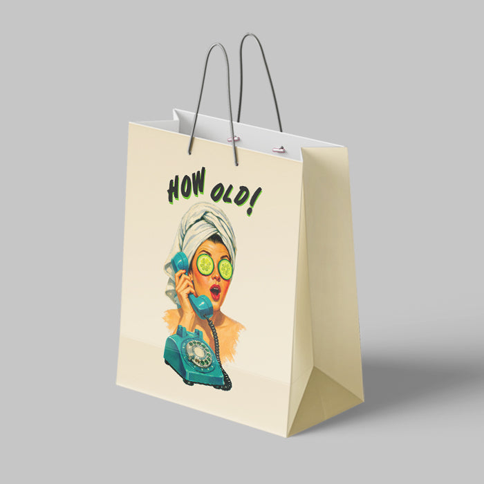 Beige paper bag with a graphic of a woman on the phone and 'How Old!' text, on a gray background