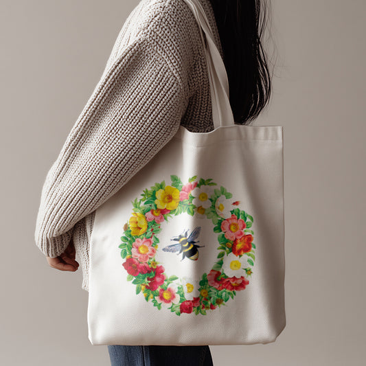 Person holding a tote bag with a floral design and bee illustration against a neutral background