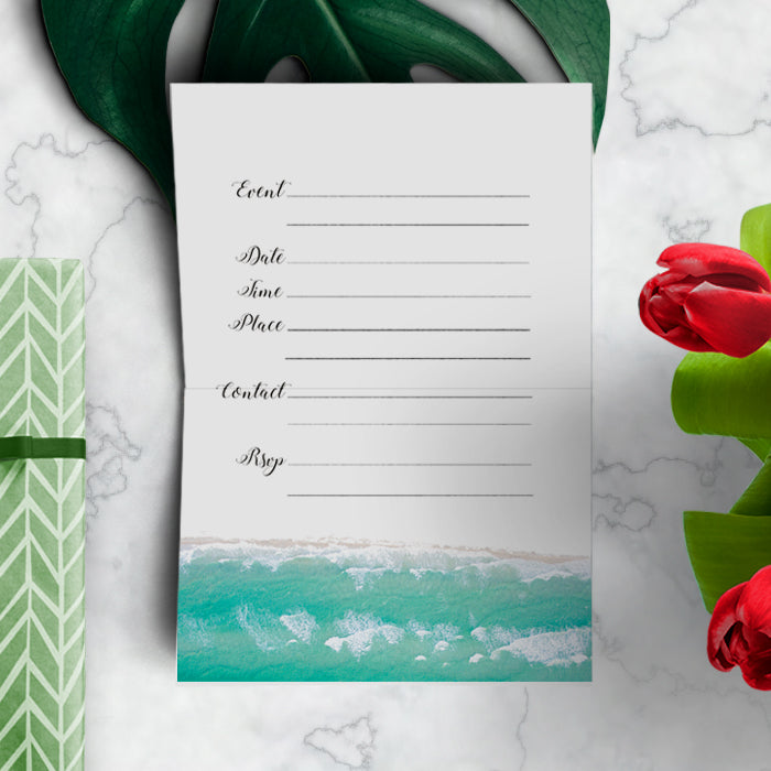 Invitation card with beach design on a marble surface with flowers and a plant.
