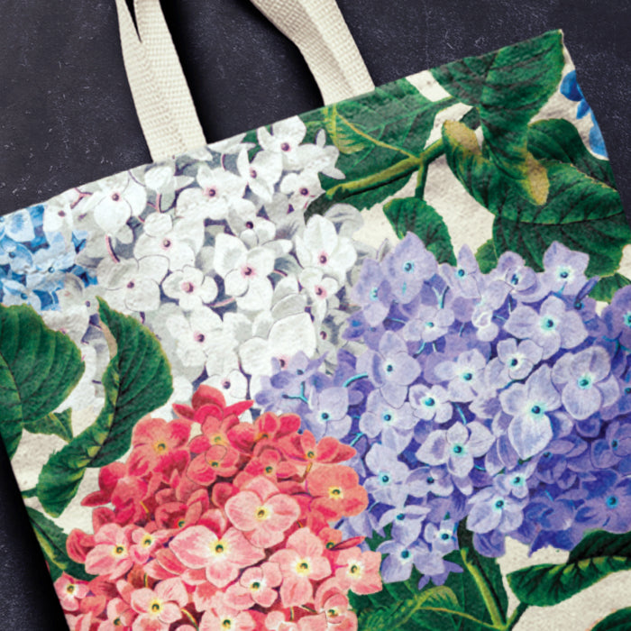 Tote bag with floral design featuring hydrangeas in various colors on a dark background.